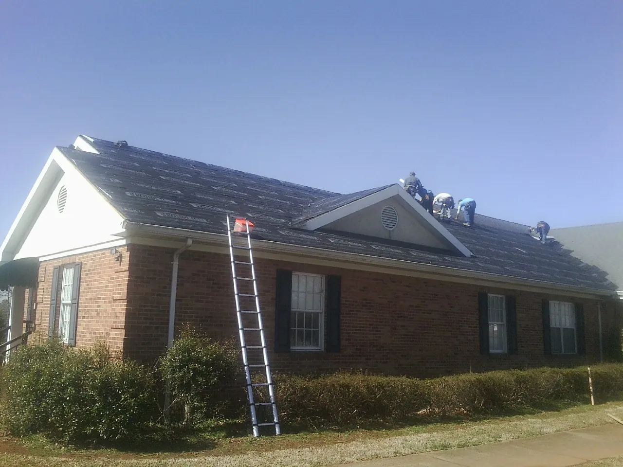 Crew tearing shingles off a brick ranch roof with a ladder set — Metal Roof Repair work by our crew in Orange